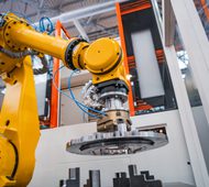 Yellow robotic arm manipulates a precision metal part inside a modern industrial production line with automation equipment and safety enclosure.